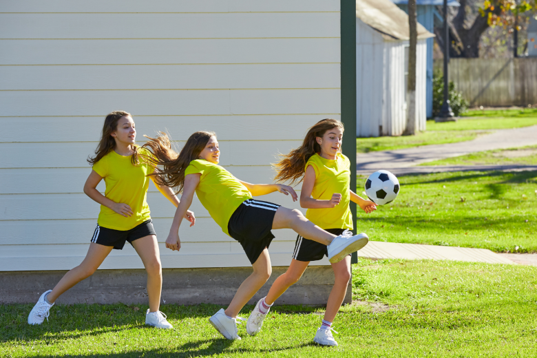 Kolme nuorta tyttöä pelaa jalkapalloa